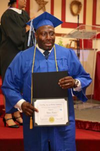 A man in a blue graduation gown holding a certificate.