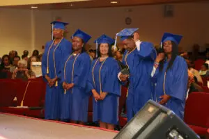 A group of people in blue graduation gowns standing in front of a podium.