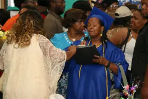 A woman in a blue graduation gown is talking to another woman.