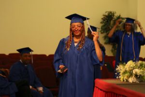 A woman in a blue graduation gown is holding a hat.
