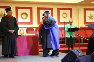 A man is hugging a woman in a graduation gown.