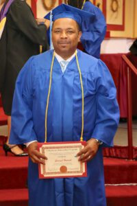 A man in a blue graduation gown holding a certificate.
