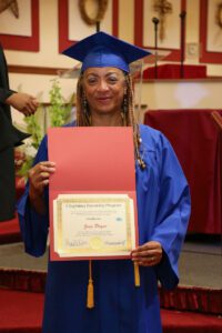 A woman in a blue graduation gown holding a certificate.