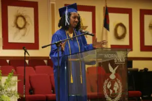 A woman in a blue graduation gown standing at a podium.