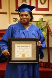 A woman in a graduation gown holding a framed certificate.