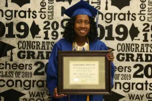 A woman holding a graduation certificate in front of a wall.